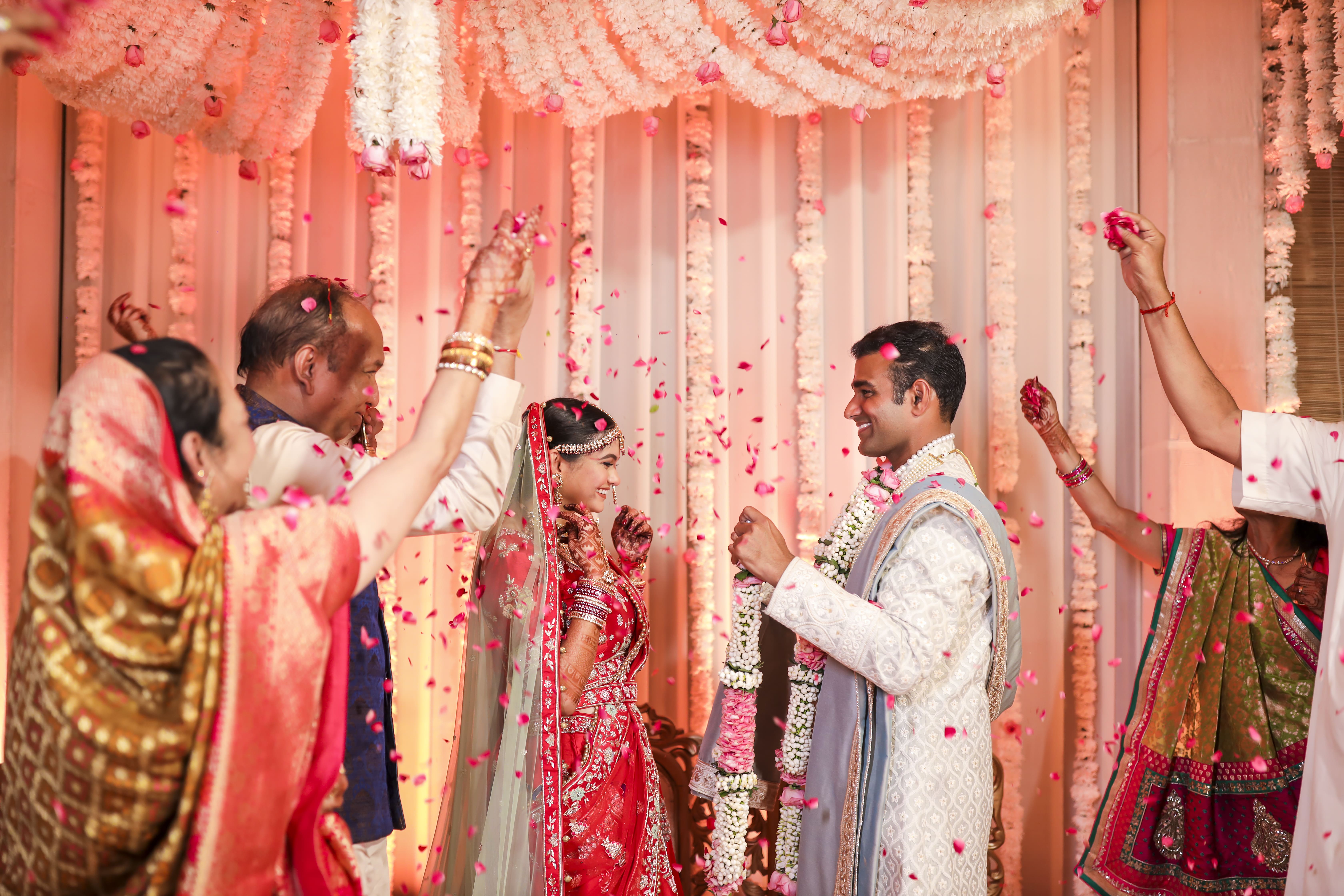 Bride and groom, poised and ready for their varmala ceremony under a floral arch.